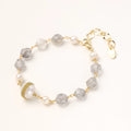 Bracelet with cloudy quartz beads, freshwater pearls, and gold-wrapped baroque pearl centerpiece on white background.