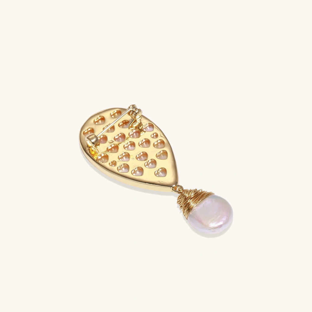 Iridescent shell brooch with gold bird accent and wire-wrapped baroque pearl drop on cream background.