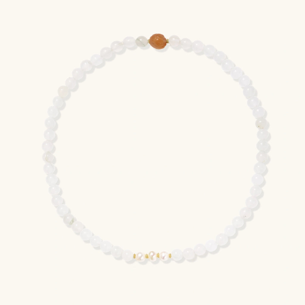 Three layered white beaded bracelets with carved orange agate lotus centerpiece and freshwater pearls on cream background.