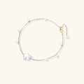 Delicate gold chain bracelet with baroque pearl centerpiece and small freshwater pearls on cream background.