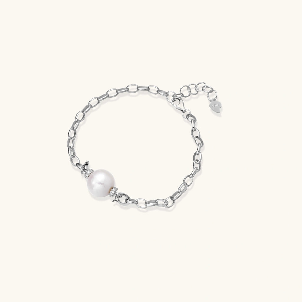 Rhodium-plated silver chain bracelet with single white freshwater pearl and heart charm clasp on cream background