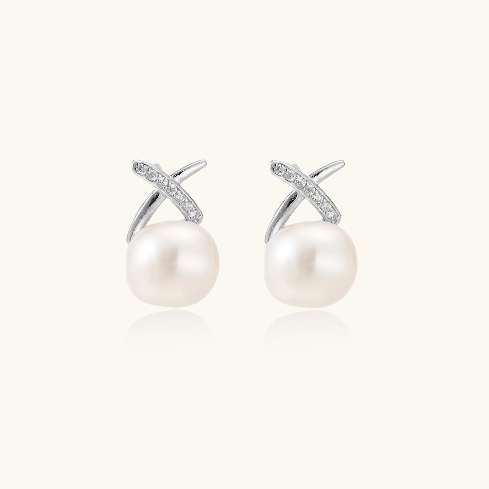 Rhodium-plated silver stud earrings with sparkling X design above lustrous round freshwater pearls on white background.