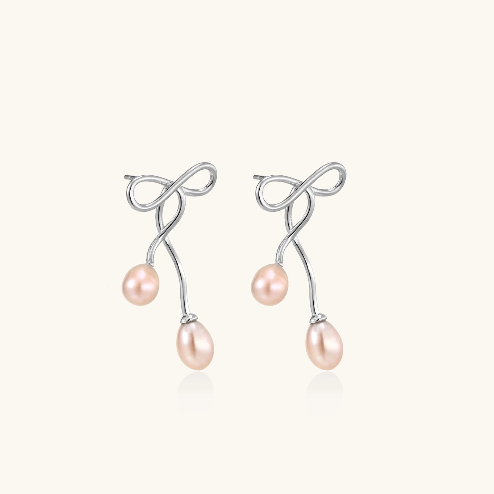 Rhodium-plated silver earrings with organic vine curves and two peachy freshwater pearls on cream background