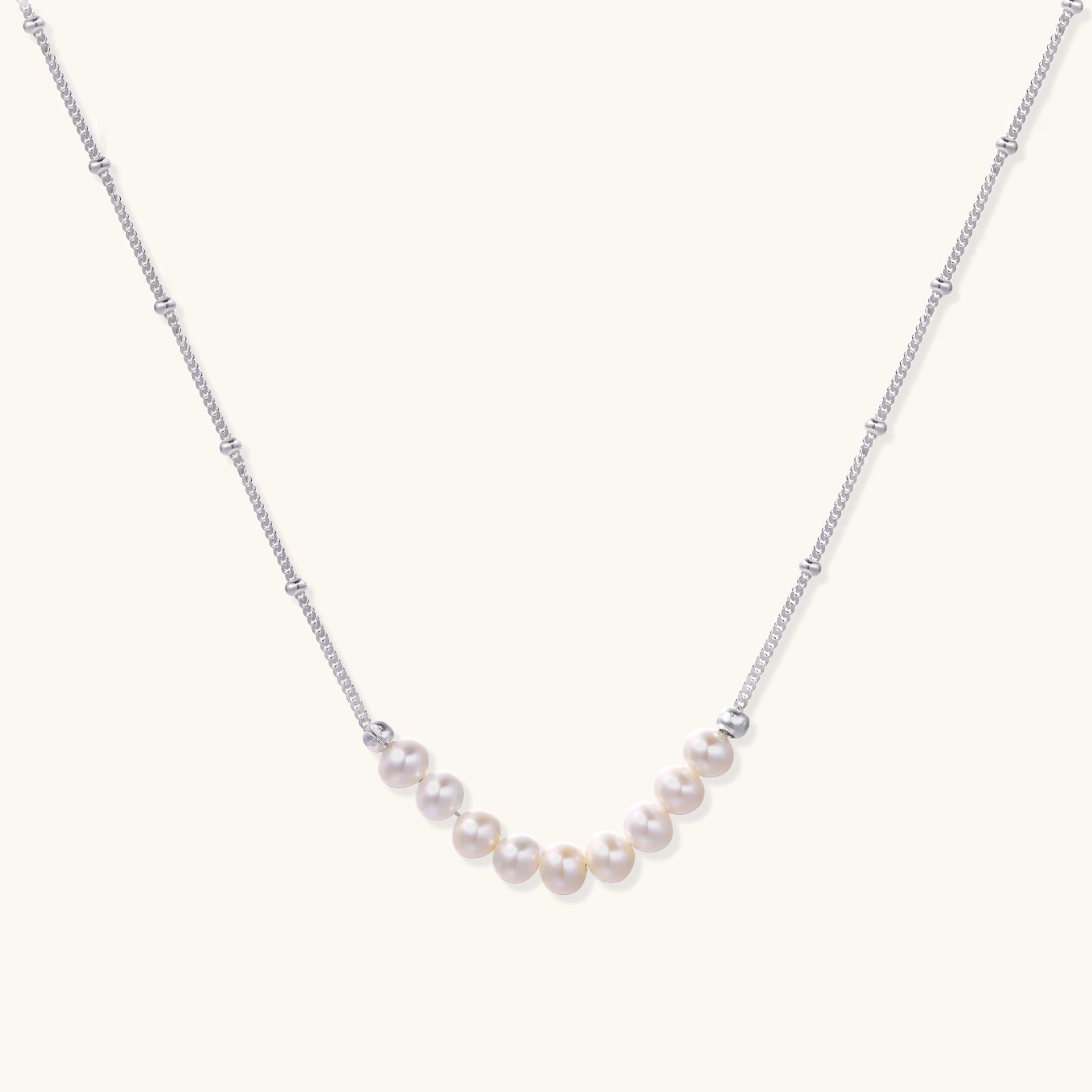 Delicate sterling silver chain necklace with small freshwater pearls arranged in a curved smile arc on cream background.