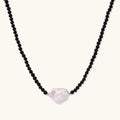 Beaded black agate necklace with iridescent baroque freshwater pearl centerpiece on cream background.