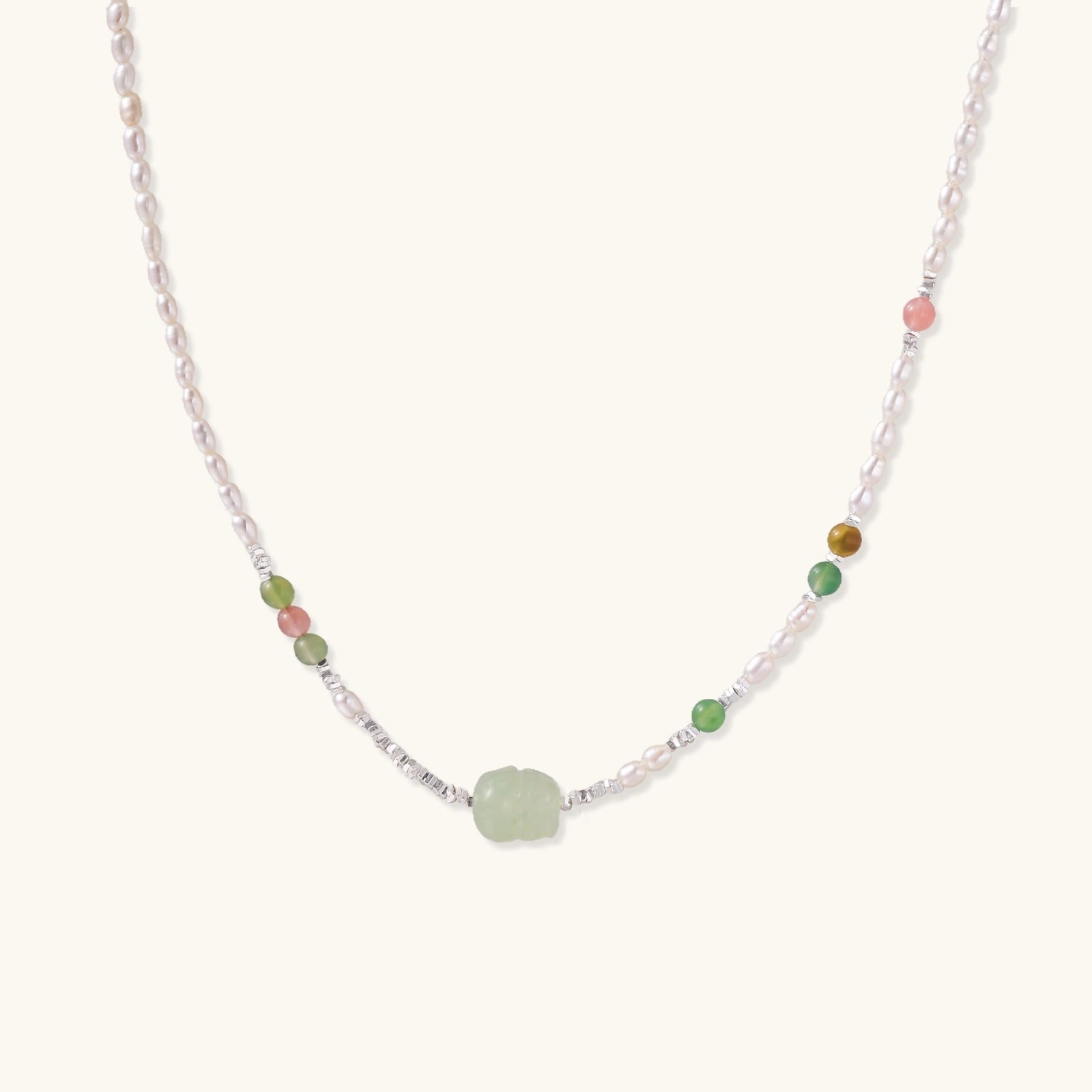 Delicate pearl necklace with pale green serpentine jade centerpiece and colorful agate beads on cream background