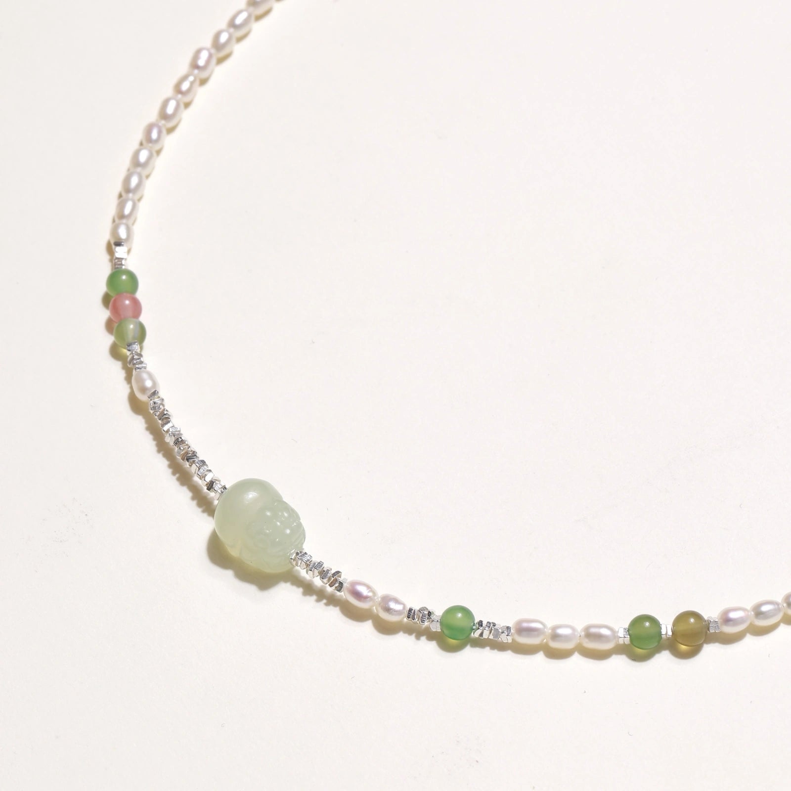 Delicate pearl necklace with pale green serpentine jade centerpiece and colorful agate beads on cream background