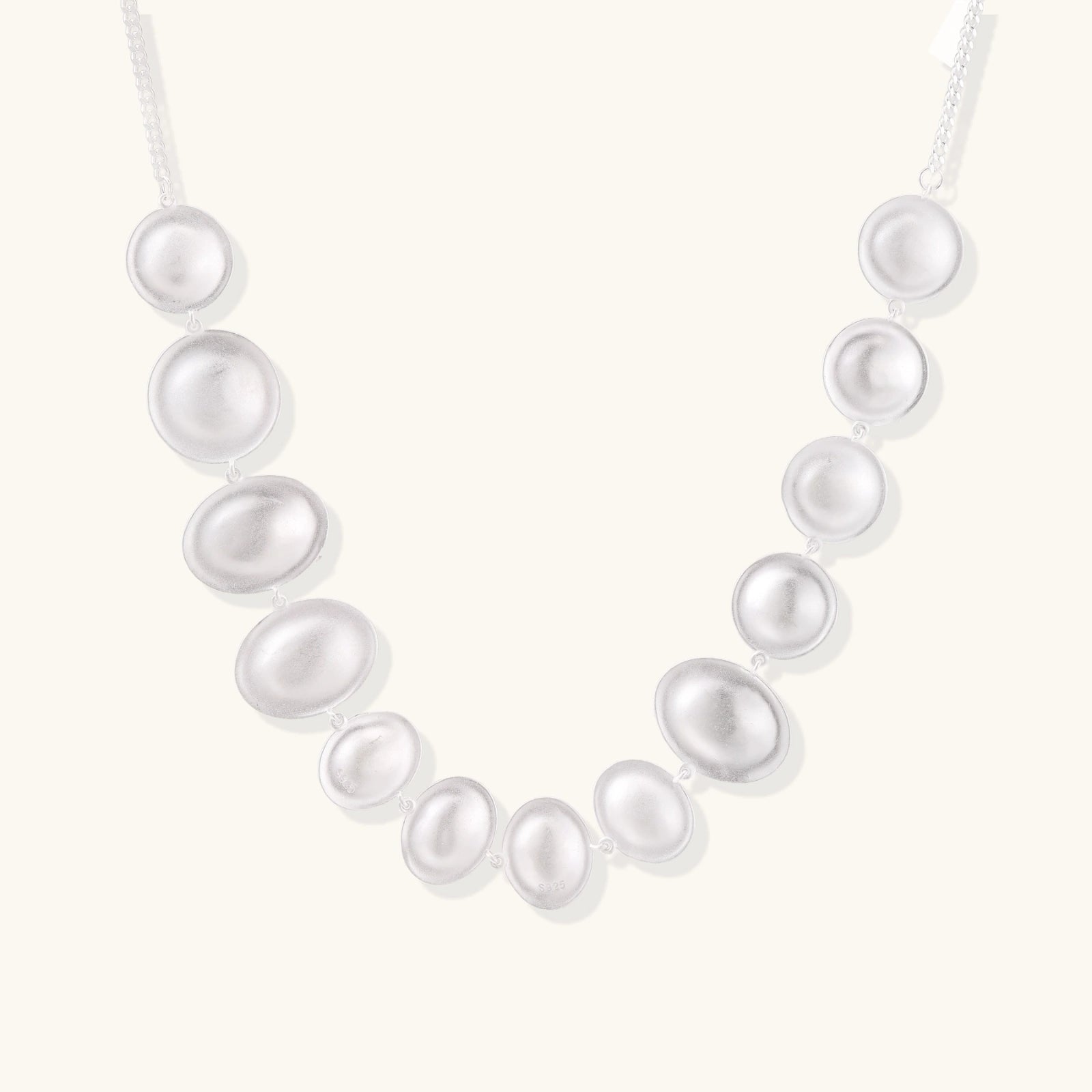 Graduated pearl-finish silver discs forming an organic bubble bib necklace on delicate chain against cream background.