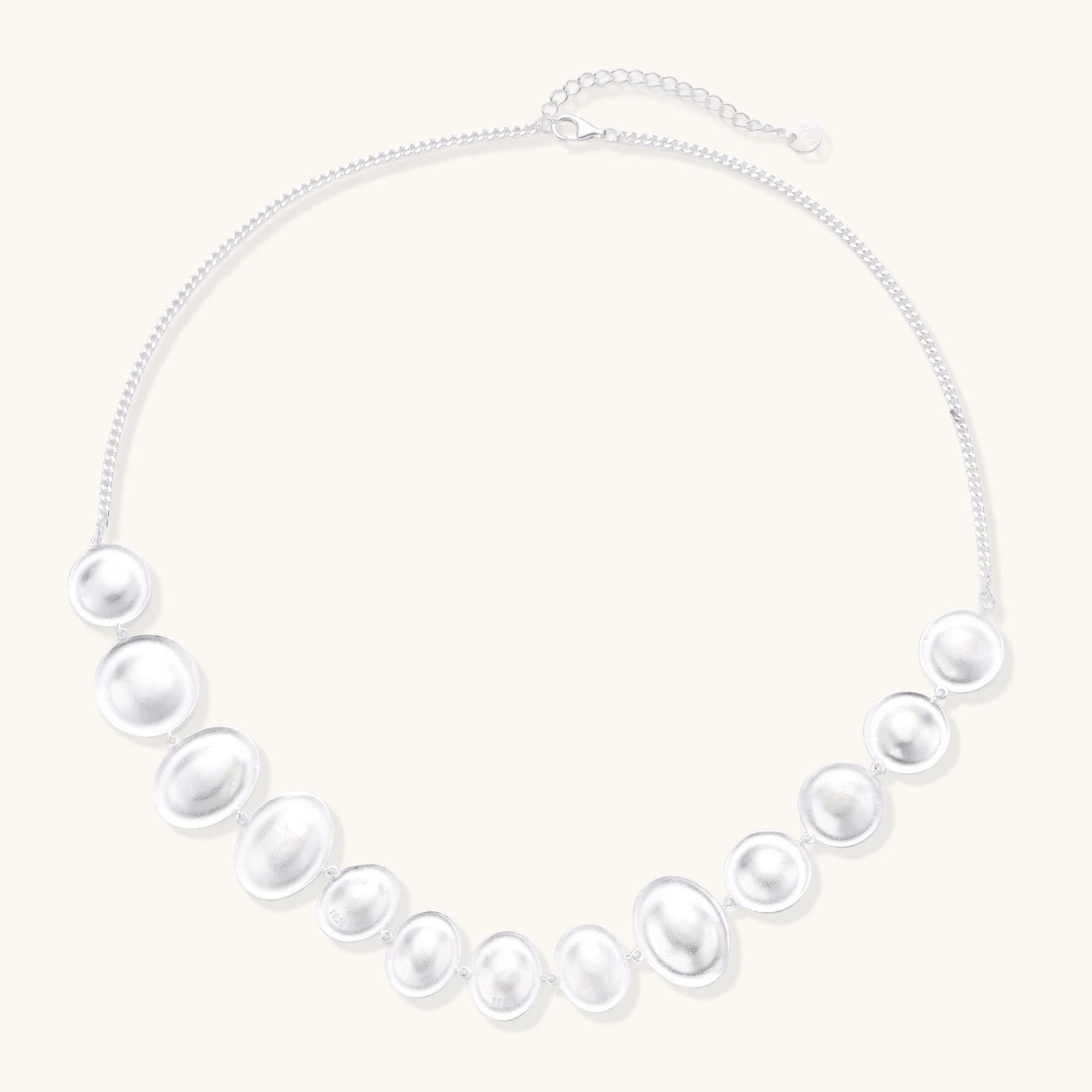 Graduated pearl-finish silver discs forming an organic bubble bib necklace on delicate chain against cream background.