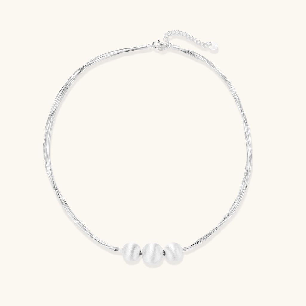 Sterling silver multi-strand necklace with three brushed round beads on cream background