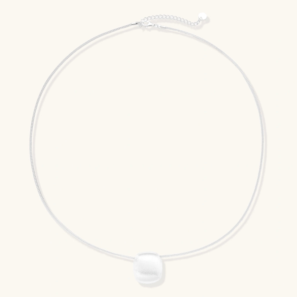 Minimalist brushed sterling silver dome pendant on delicate chain against cream background, showing matte textured finish