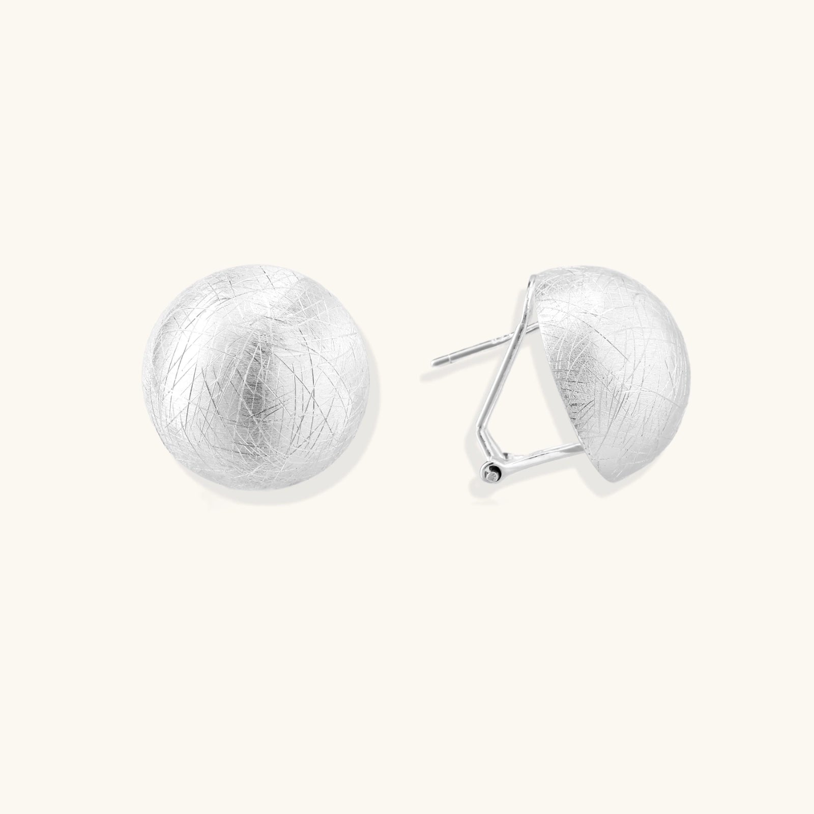 Brushed sterling silver half-dome clip-on earrings with textured surface against cream background