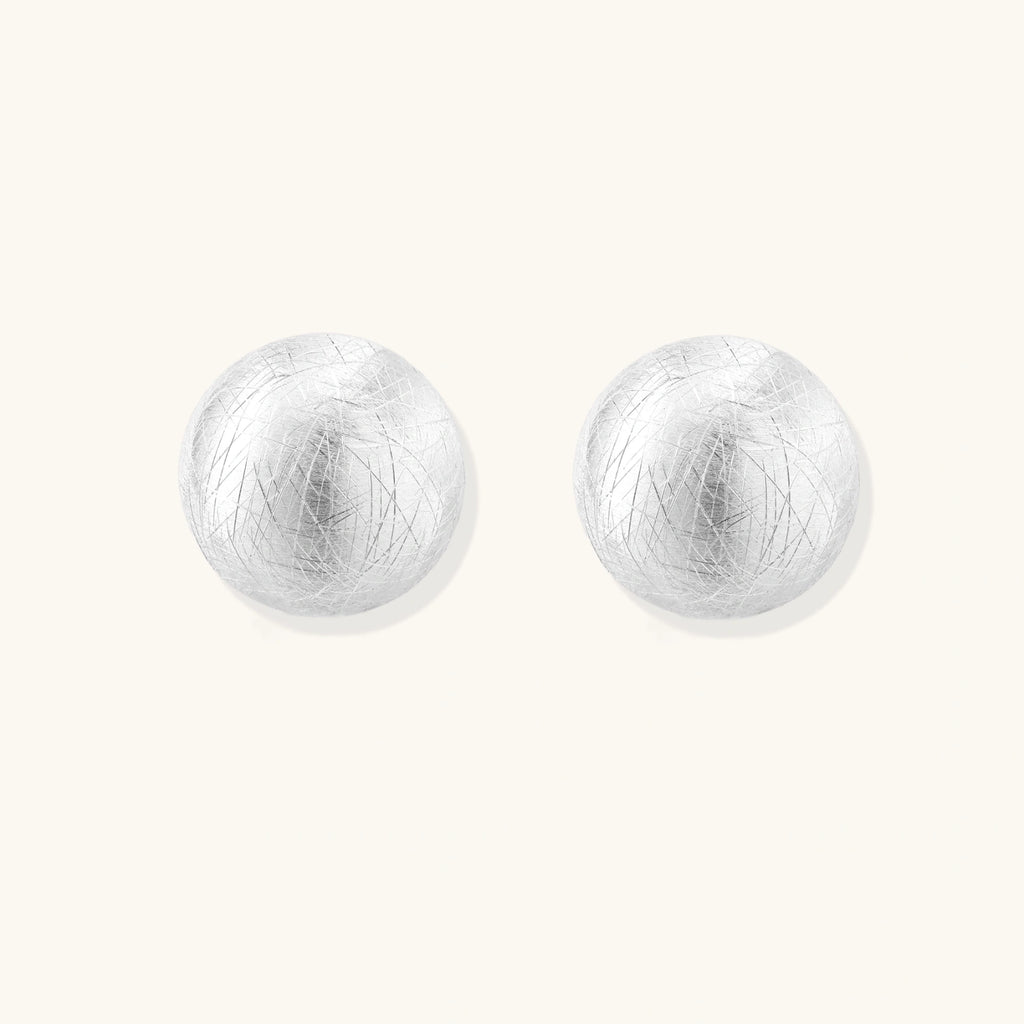 Brushed sterling silver half-dome clip-on earrings with textured surface against cream background