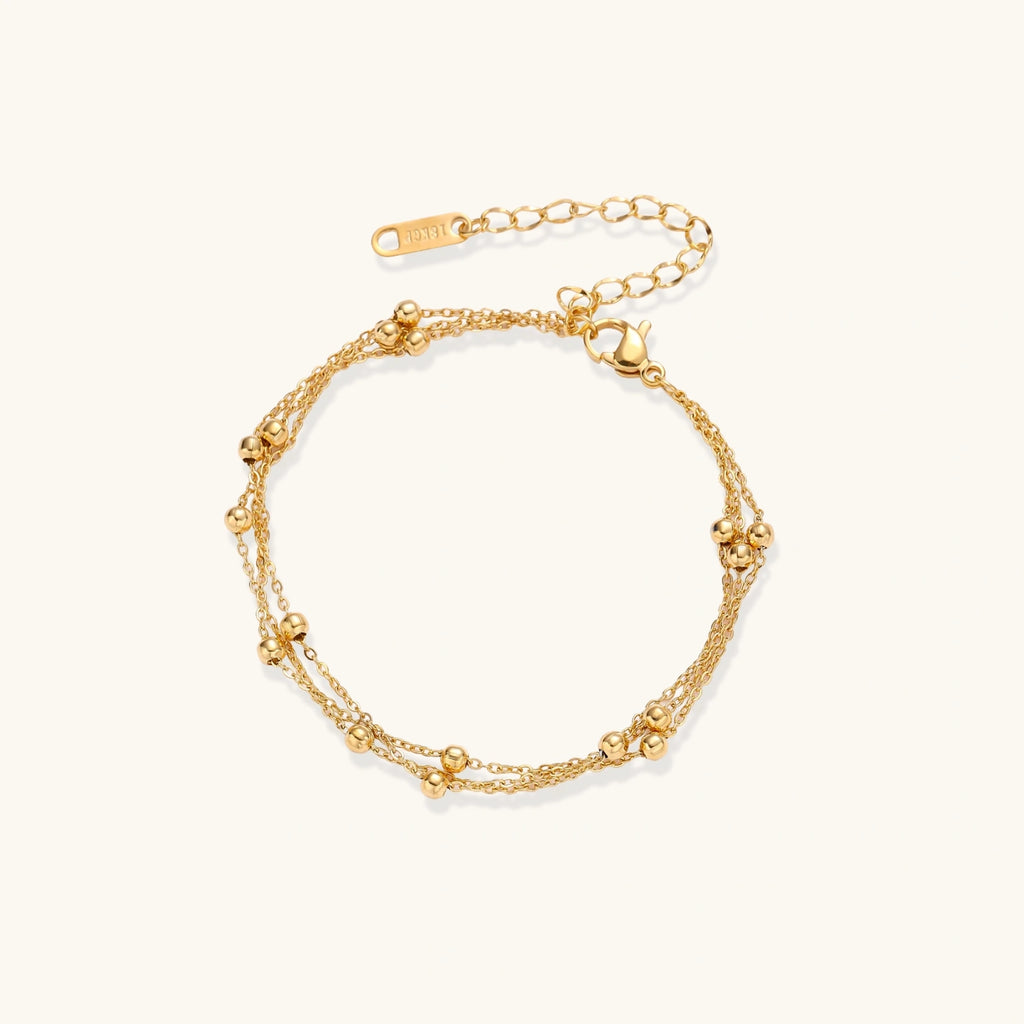 Three-strand gold-plated bracelet with clustered ball beads and adjustable clasp on cream background