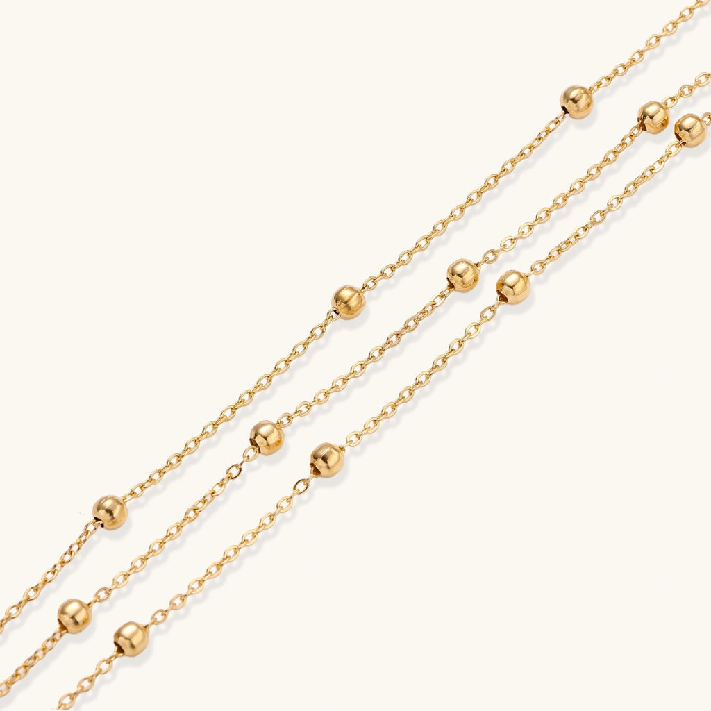 Three-strand gold-plated bracelet with clustered ball beads and adjustable clasp on cream background