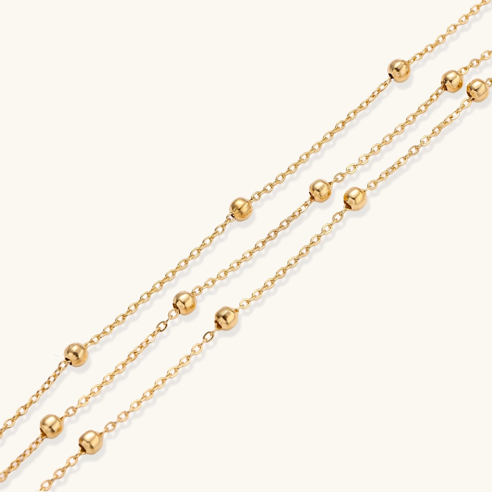Three-strand gold-plated bracelet with clustered ball beads and adjustable clasp on cream background