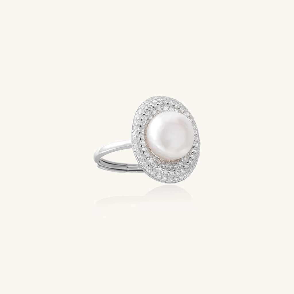 Silver ring with lustrous white pearl center surrounded by sparkling crystal halo on light background.