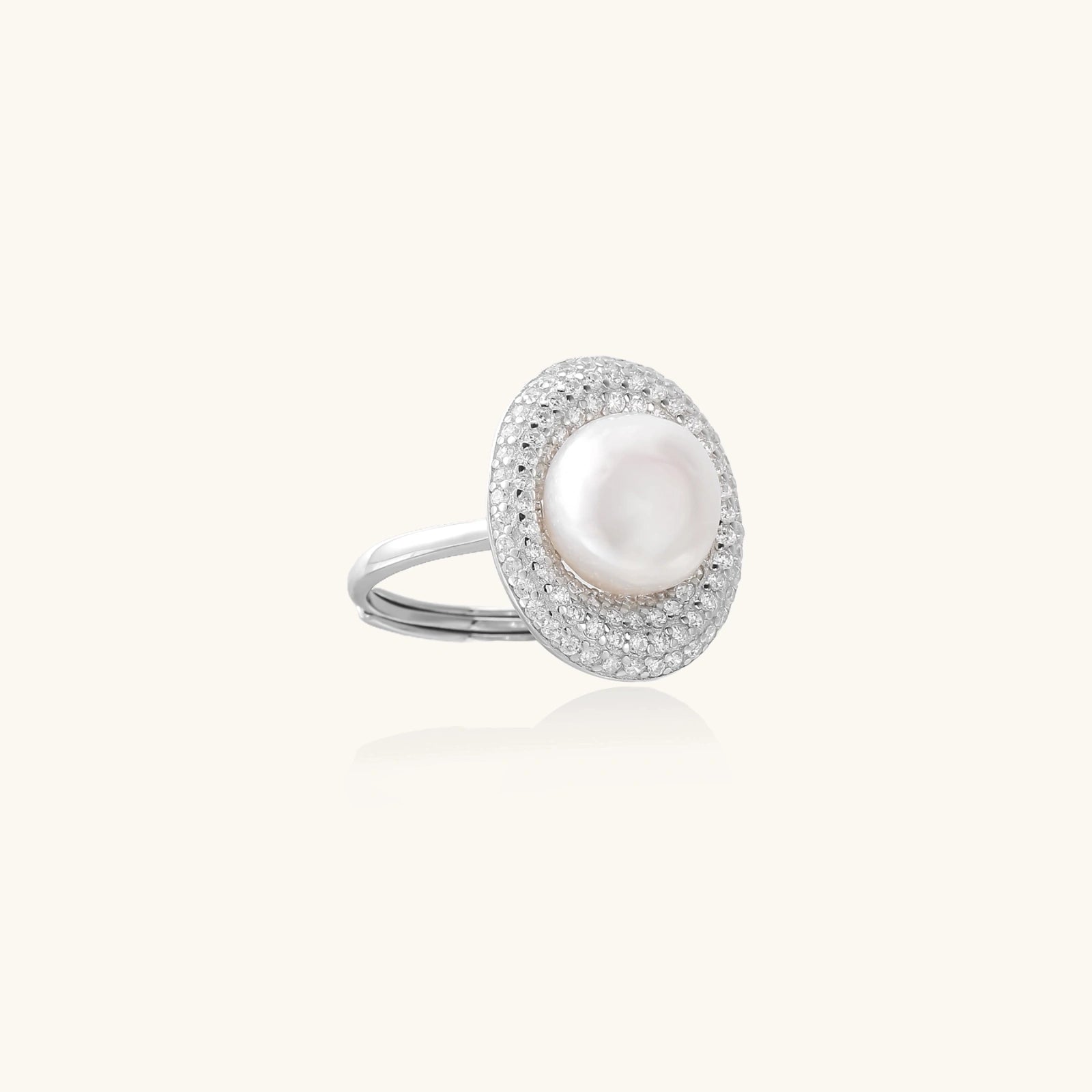 Silver ring with lustrous white pearl center surrounded by sparkling crystal halo on light background.