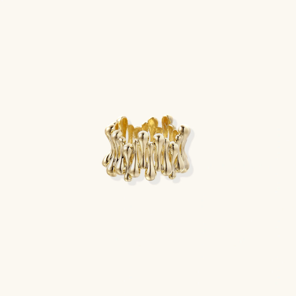 Gold-plated brass ring with sculptural petal-like elements in a wide band design on beige background