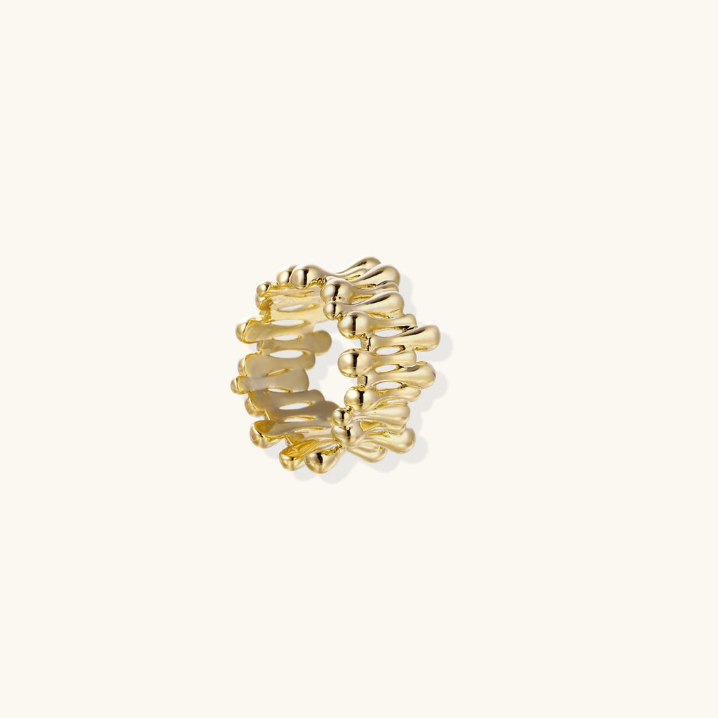 Gold-plated brass ring with sculptural petal-like elements in a wide band design on beige background