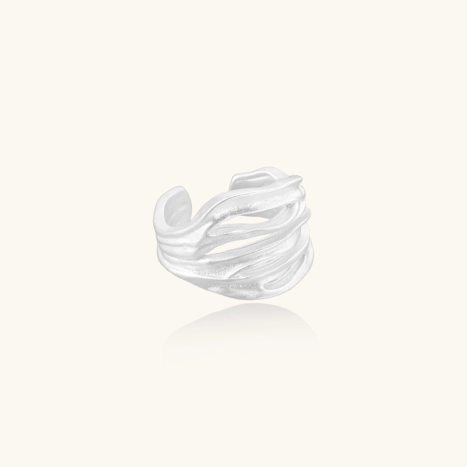 Wide sterling silver cuff ring with flowing wave patterns creating dimensional texture against cream background